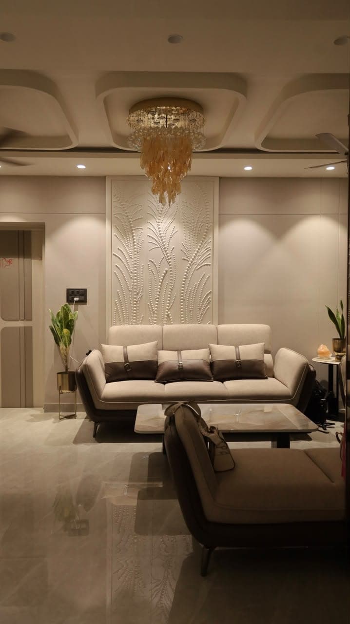 A living room by Stylescape Studio — cream sofas beneath a sculpted feather-pattern feature wall and a cascading capiz-shell chandelier, on a polished marble floor
