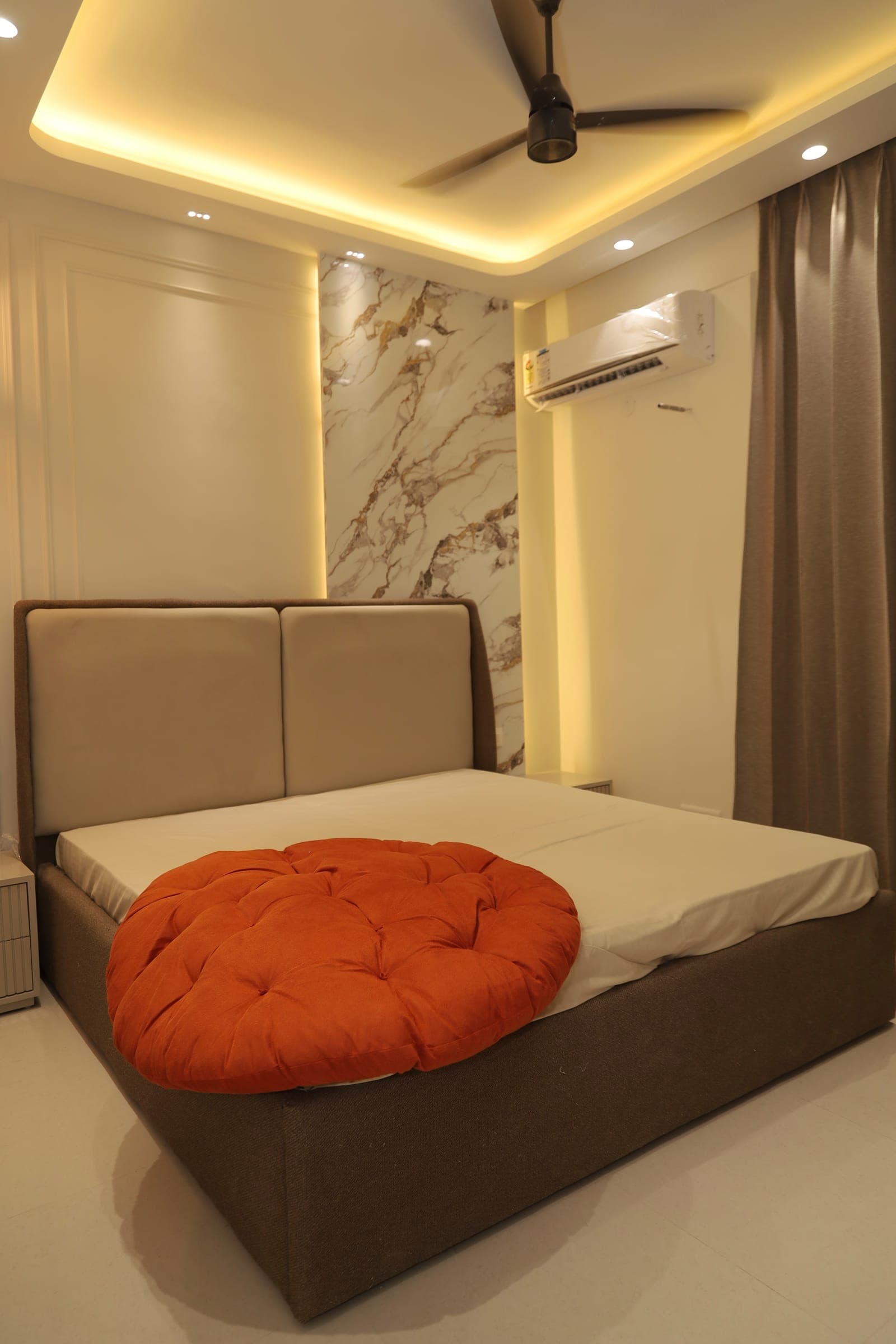 Bedroom with a grey upholstered bed, a veined marble accent wall and recessed cove lighting.